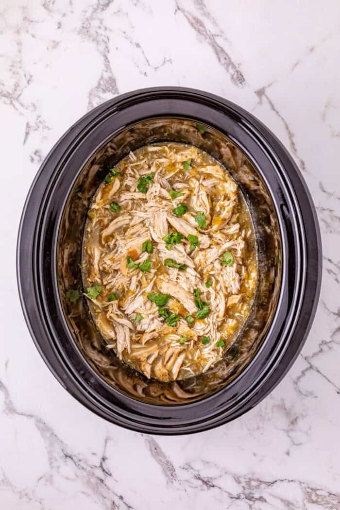 Chicken breast is slow cooked in salsa verde then shredded to make this Crockpot Salsa Verde Chicken. Easy dinner idea! Overhead view of salsa verde chicken in the crockpot