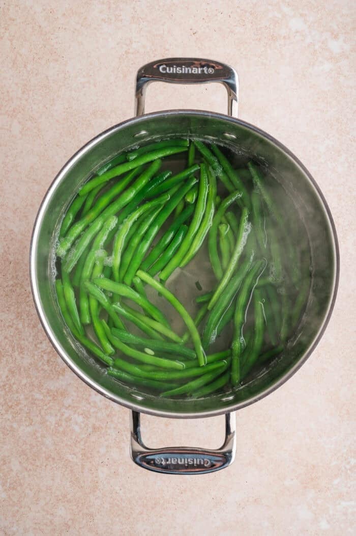 These Green Beans Almondine are a quick and easy side dish made with tender crisp green beans, buttery shallots, and toasted almonds. Green beans blanching in a pot of water