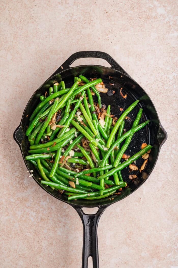 These Green Beans Almondine are a quick and easy side dish made with tender crisp green beans, buttery shallots, and toasted almonds. Overhead view of green beans almondine in a skillet