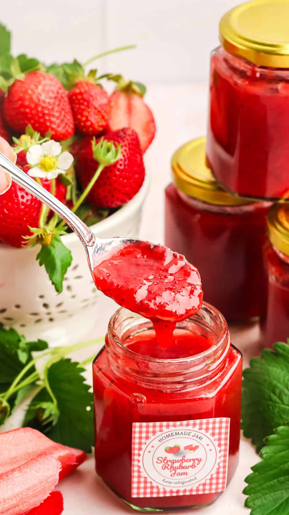A spoonful of strawberry rhubarb jam over the jar in front of other jars
