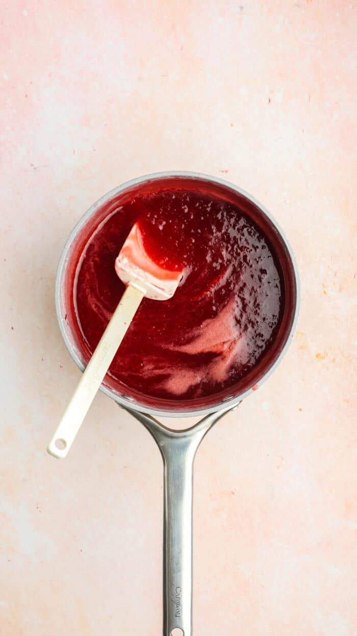 A spatula stirring strawberry rhubarb jam in the pan