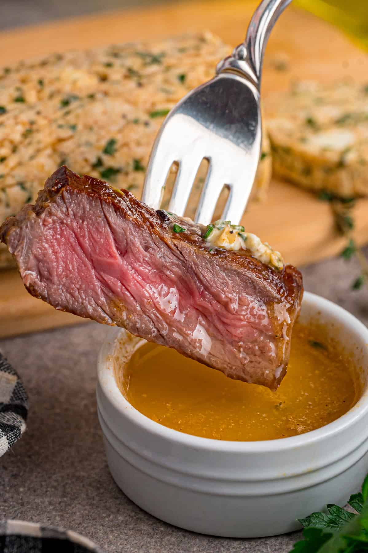 A fork dipping a piece of steak into melted cowboy butter