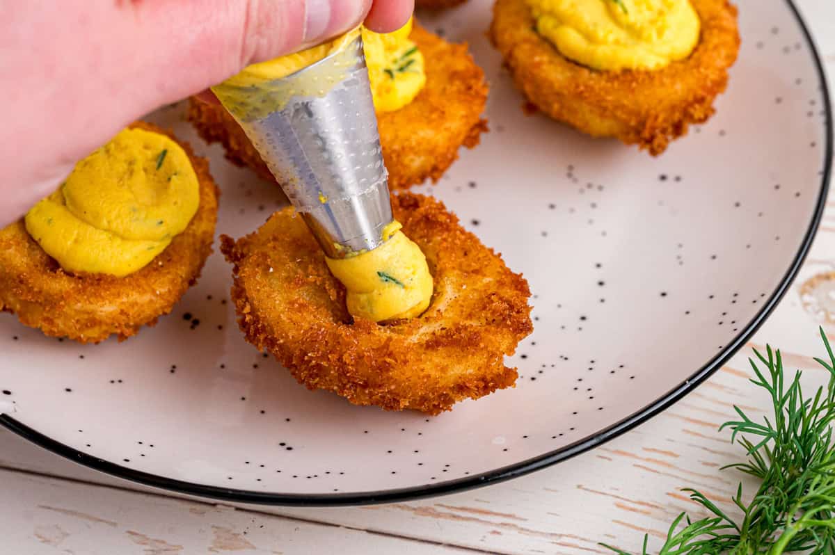 Fried Deviled Eggs are a fun twist on the classic, with hard-boiled egg whites coated in breadcrumbs and deep-fried. Piping fried deviled eggs with egg yolk filling
