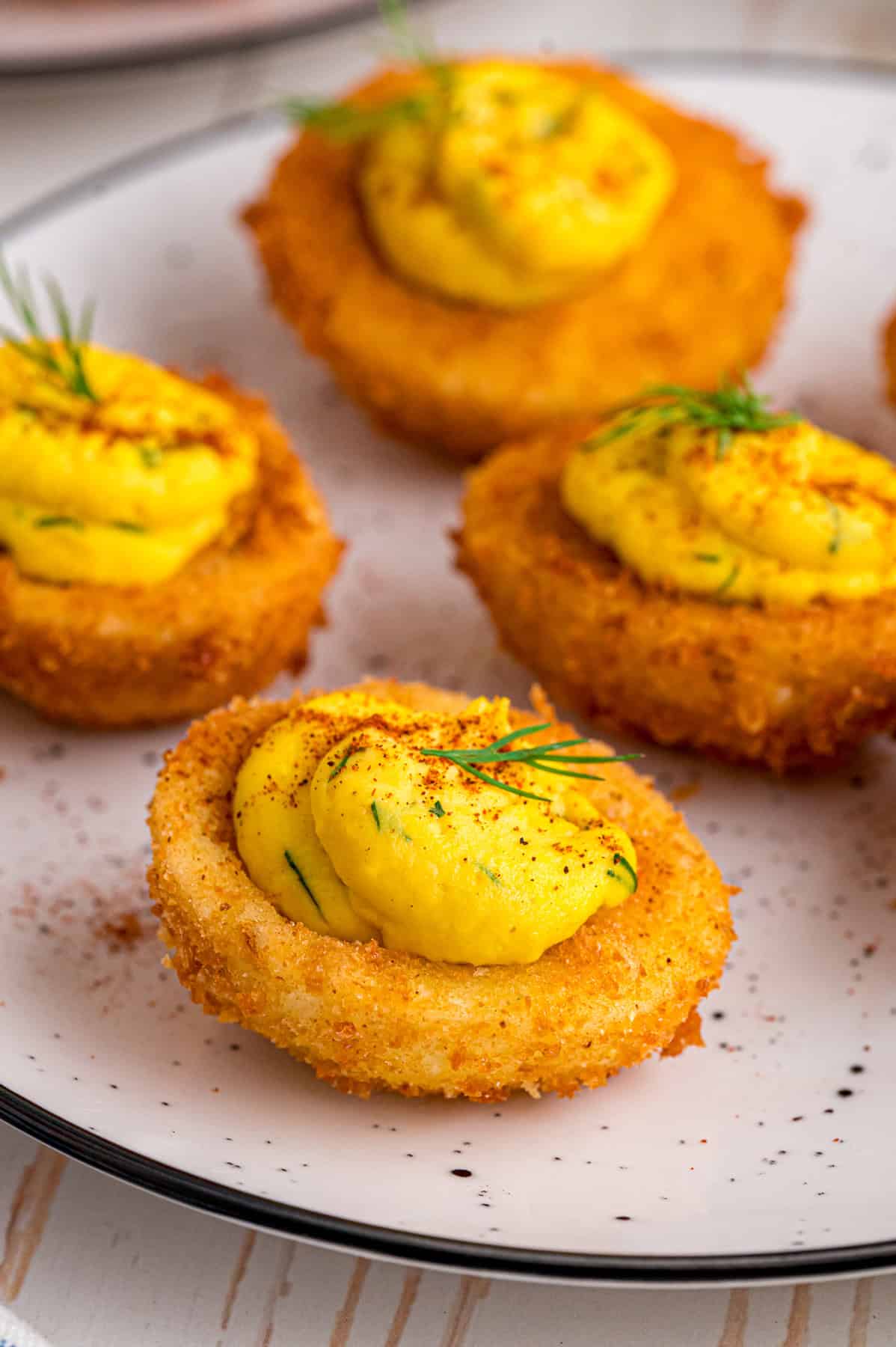 Fried Deviled Eggs are a fun twist on the classic, with hard-boiled egg whites coated in breadcrumbs and deep-fried. Close up of fried deviled eggs on a white plate