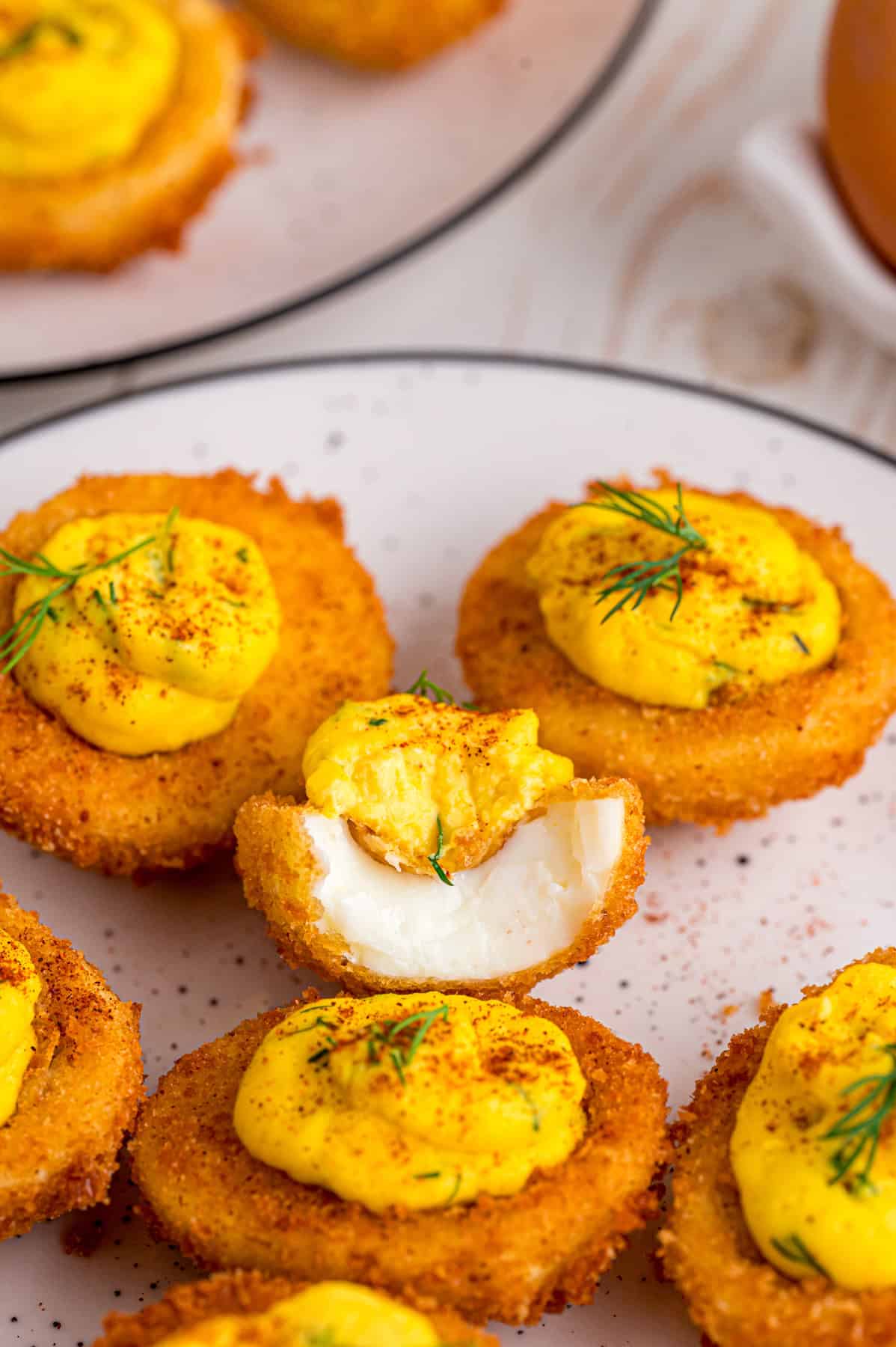 Fried Deviled Eggs are a fun twist on the classic, with hard-boiled egg whites coated in breadcrumbs and deep-fried. A plate of fried deviled eggs, one with a bite missing