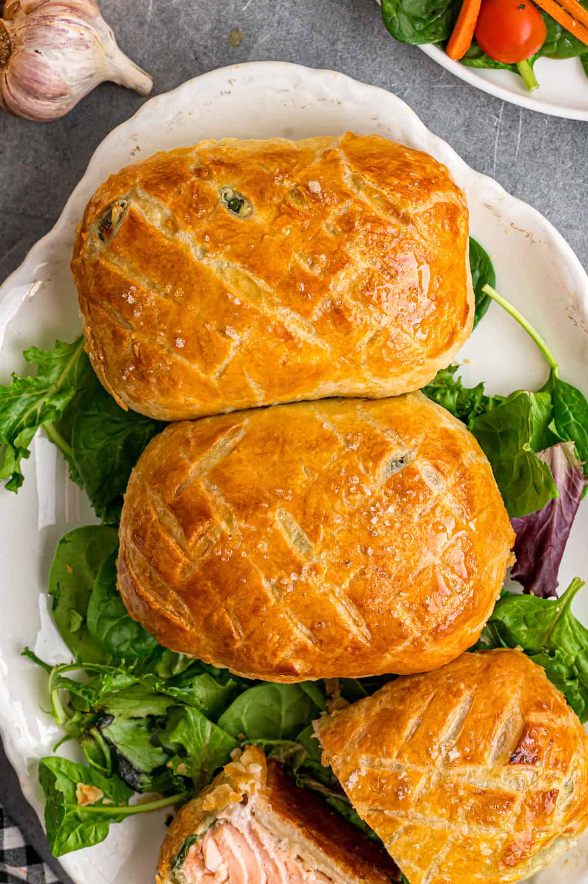 This Salmon Wellington recipe features tender salmon topped with a cream cheese spinach filling and wrapped in a flaky puff pastry. Overhead view of three salmon wellington on a platter