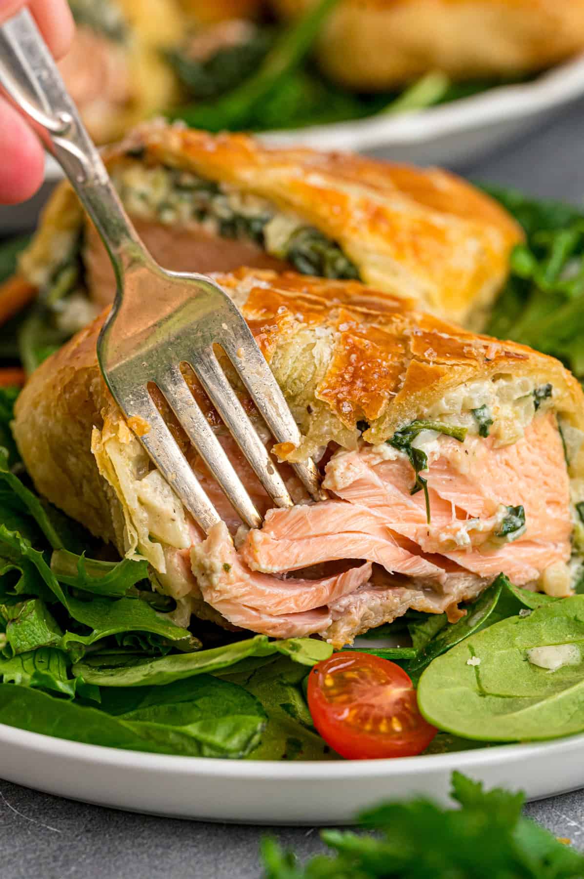 This Salmon Wellington recipe features tender salmon topped with a cream cheese spinach filling and wrapped in a flaky puff pastry. A fork diving into a salmon wellington