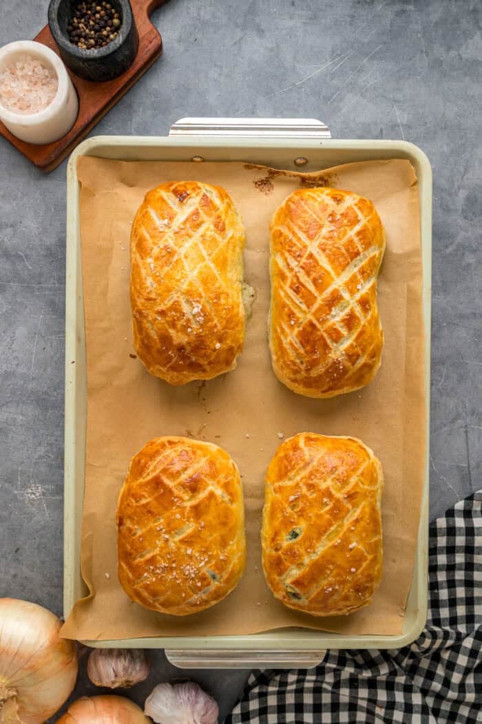 This Salmon Wellington recipe features tender salmon topped with a cream cheese spinach filling and wrapped in a flaky puff pastry. Four salmon wellington on a baking sheet.