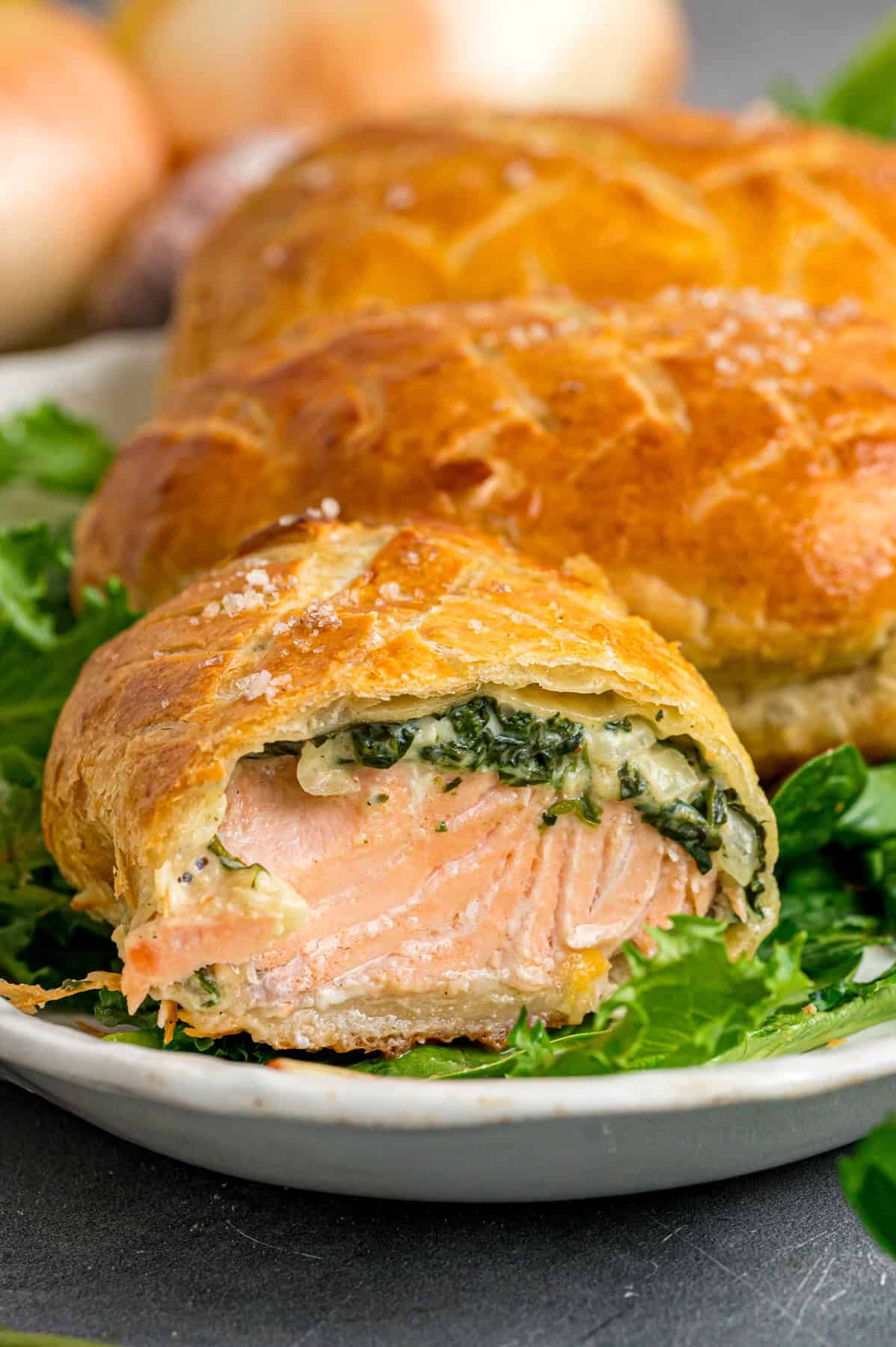 This Salmon Wellington recipe features tender salmon topped with a cream cheese spinach filling and wrapped in a flaky puff pastry. Two salmon wellingtons on a plate, one cut to show the inside