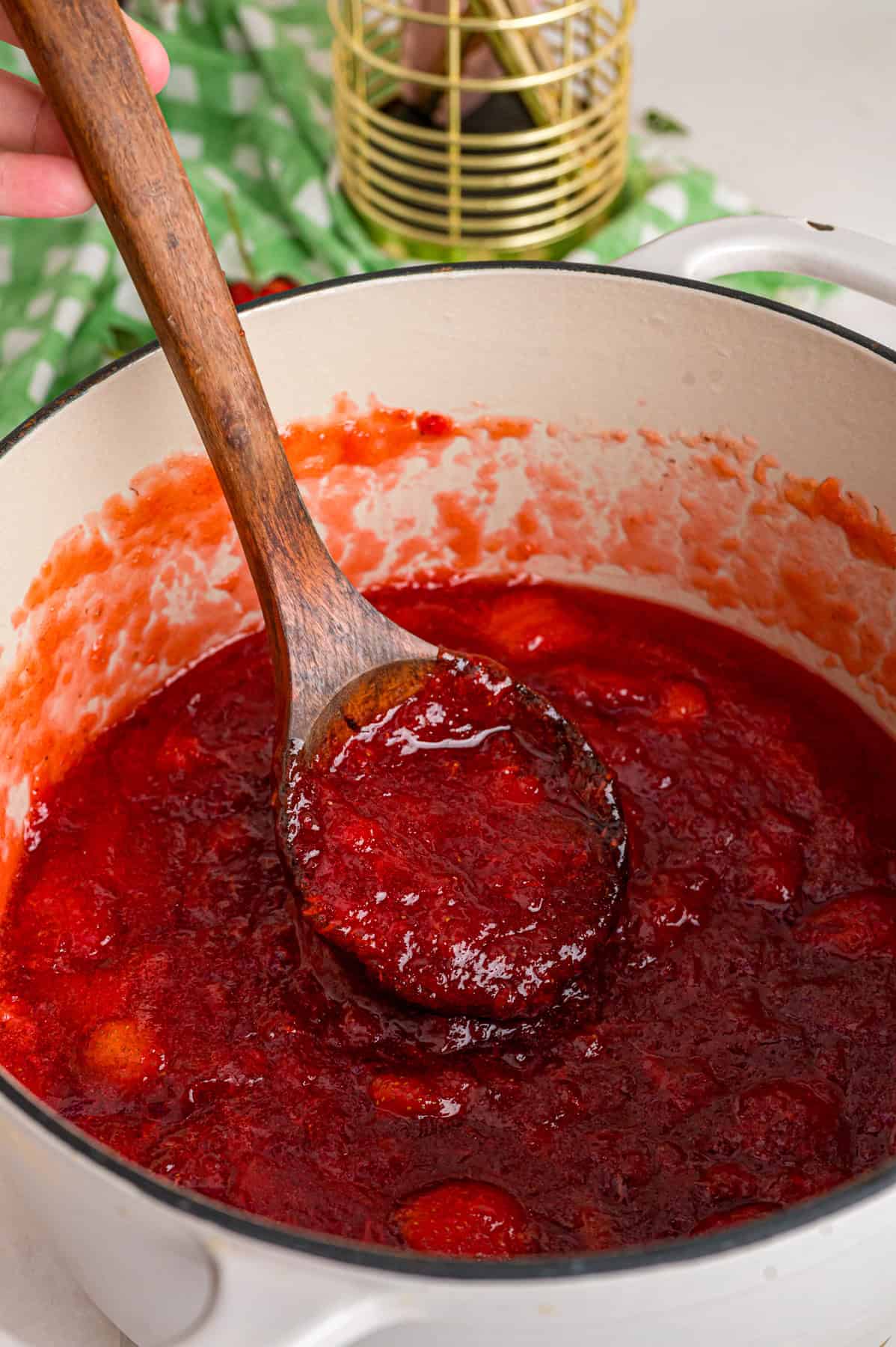 Made with just 4 ingredients, this Strawberry Jam recipe is quick and easy to make with no canning equipment required. A wooden spoon stirring strawberry jam