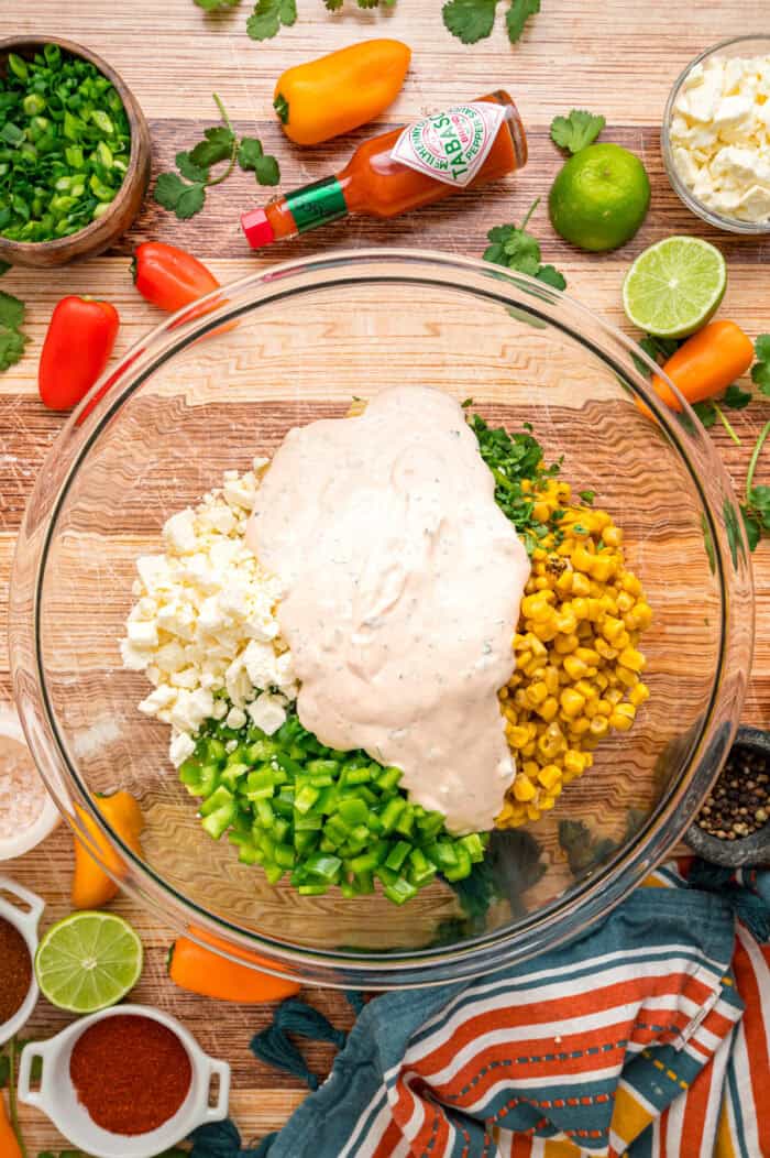 Charred corn kernels, feta cheese, and pasta are tossed in a creamy dressing to make this Street Corn Pasta Salad. Dressing added to a bowl of pasta, green onions, and charred corn kernels