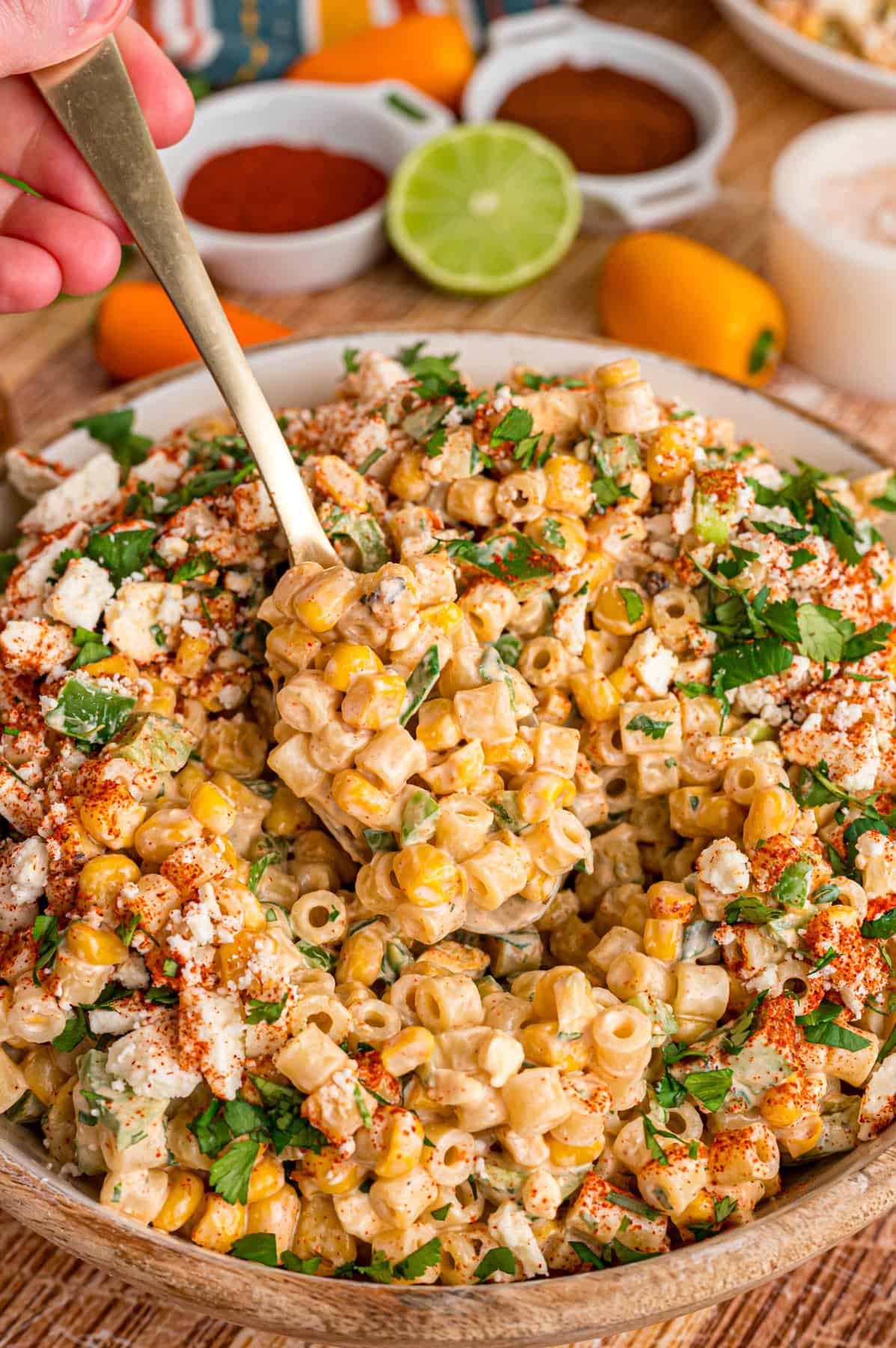 Charred corn kernels, cotija cheese, and pasta are tossed in a creamy dressing to make this Street Corn Pasta Salad. A hand holding a spoon in a bowl of street corn pasta salad