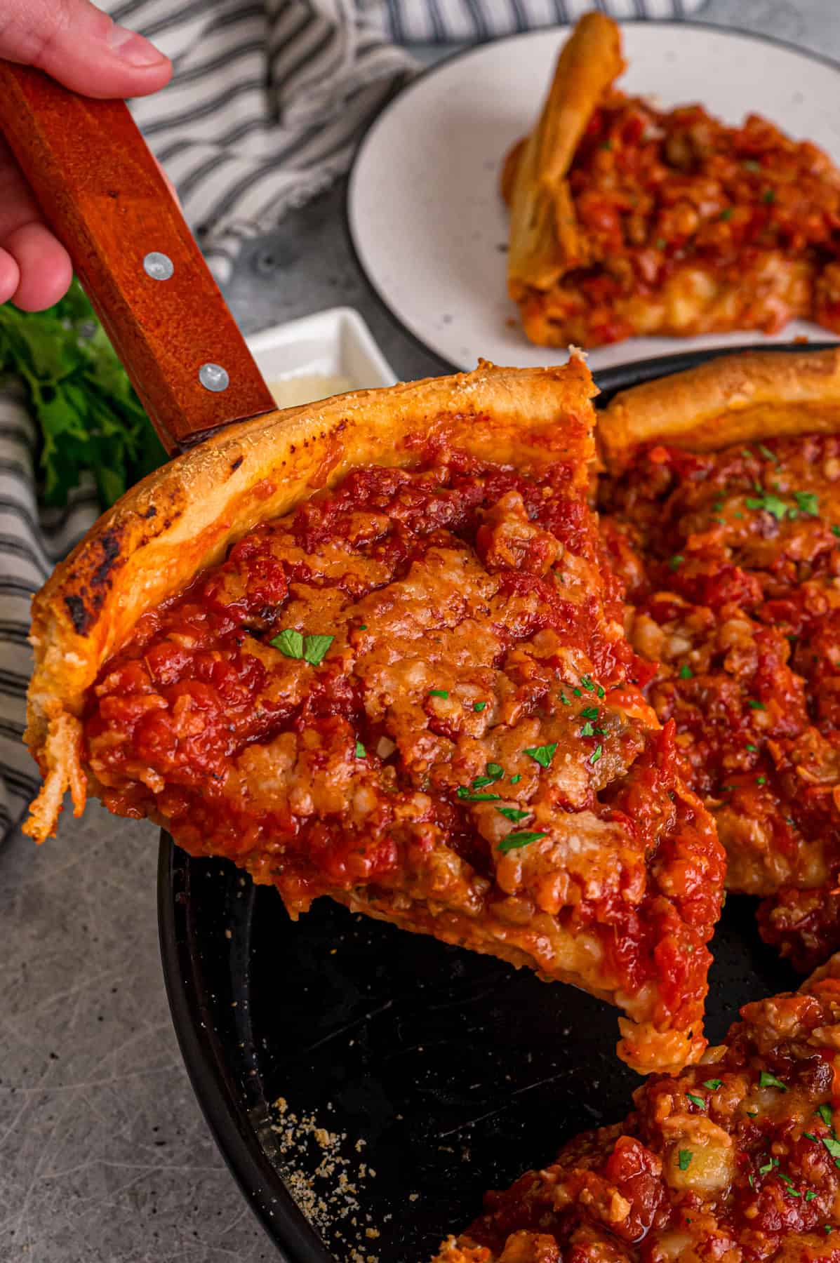 This Chicago-Style Deep Dish Pizza recipe features a buttery, flaky crust topped with mozzarella, crumbled sausage, & a savory tomato sauce. A slice of Chicago deep dish pizza on a spatula