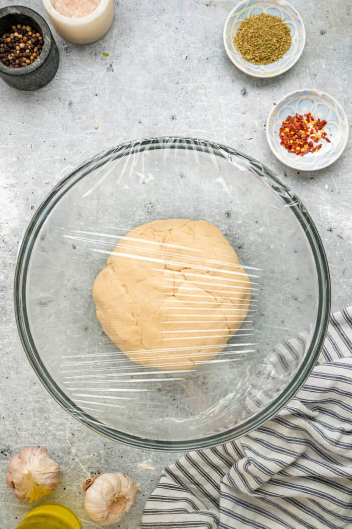 This Chicago-Style Deep Dish Pizza recipe features a buttery, flaky crust topped with mozzarella, crumbled sausage, & a savory tomato sauce. A ball of pizza dough covered in a bowl