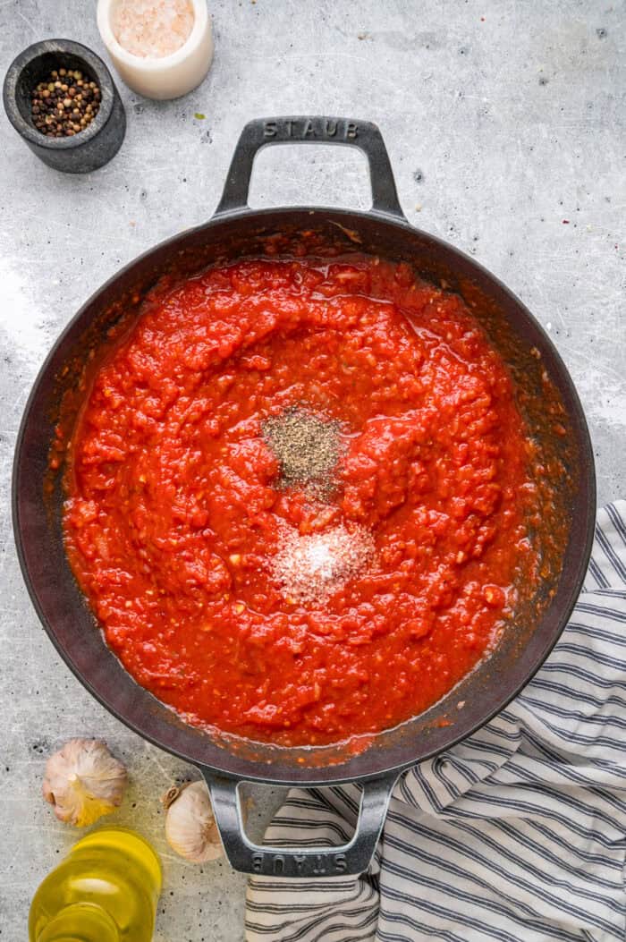 This Chicago-Style Deep Dish Pizza recipe features a buttery, flaky crust topped with mozzarella, crumbled sausage, & a savory tomato sauce. Spices added to crushed tomatoes in a pan
