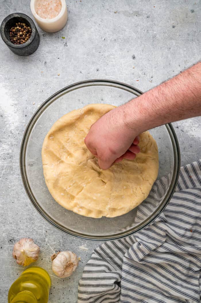 A hand punching down pizza dough after it's risen