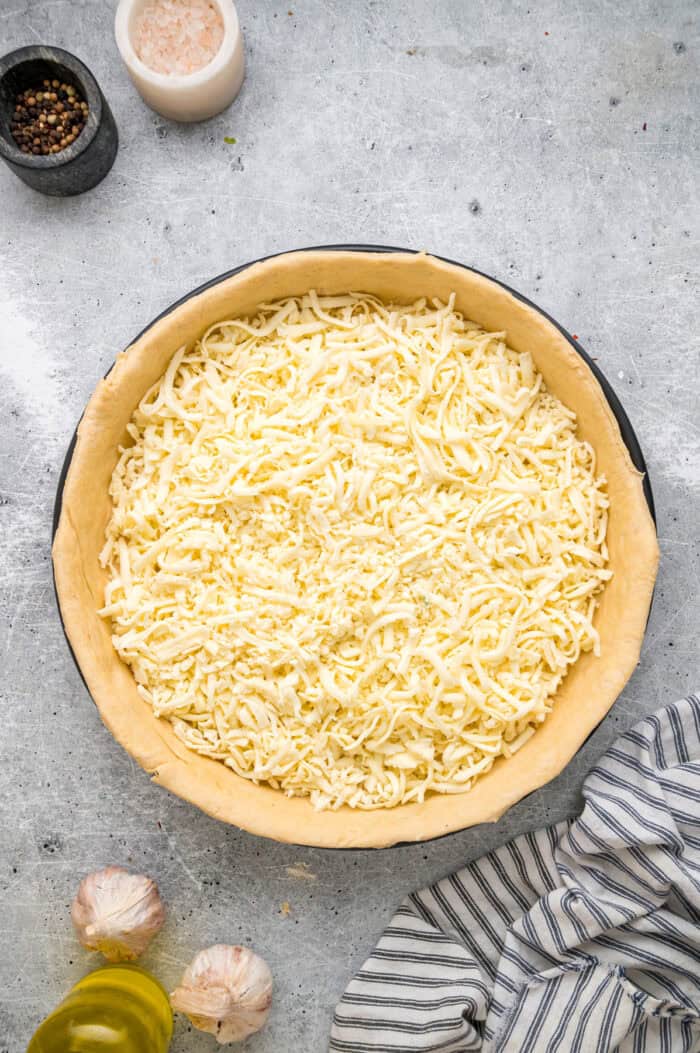 This Chicago-Style Deep Dish Pizza recipe features a buttery, flaky crust topped with mozzarella, crumbled sausage, & a savory tomato sauce. Mozzarella cheese spread on top of pizza dough