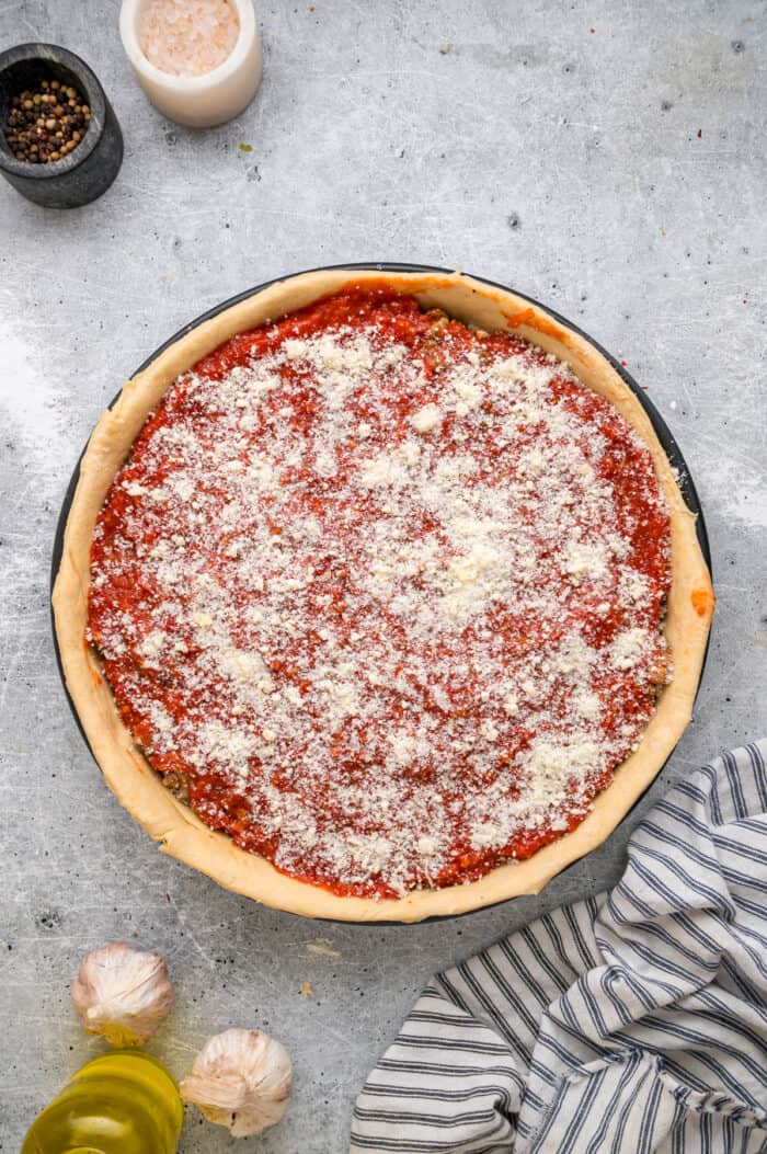 This Chicago-Style Deep Dish Pizza recipe features a buttery, flaky crust topped with mozzarella, crumbled sausage, & a savory tomato sauce. Pizza sauce spread over the toppings and topped with parmesan