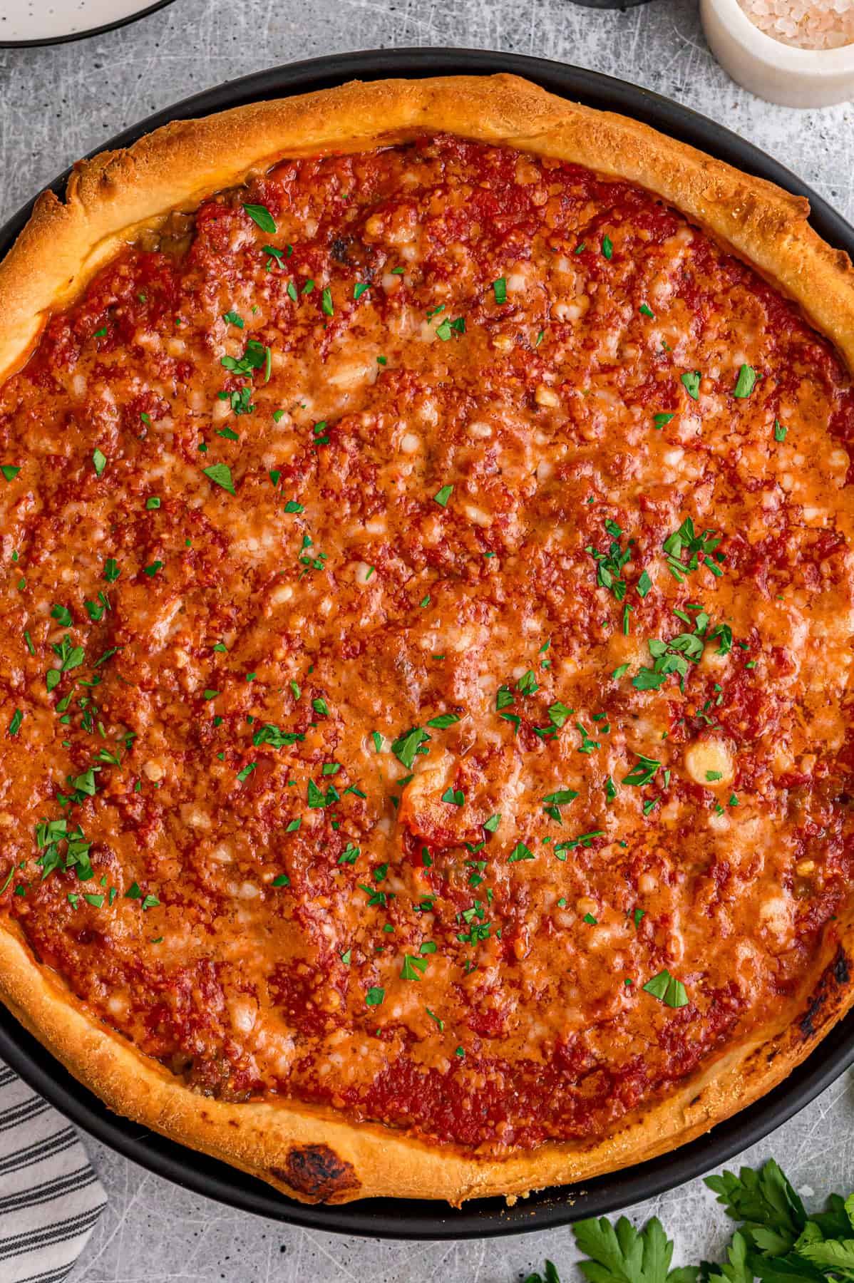 This Chicago-Style Deep Dish Pizza recipe features a buttery, flaky crust topped with mozzarella, crumbled sausage, & a savory tomato sauce. Overhead view of a pan of Chicago-style deep dish pizza