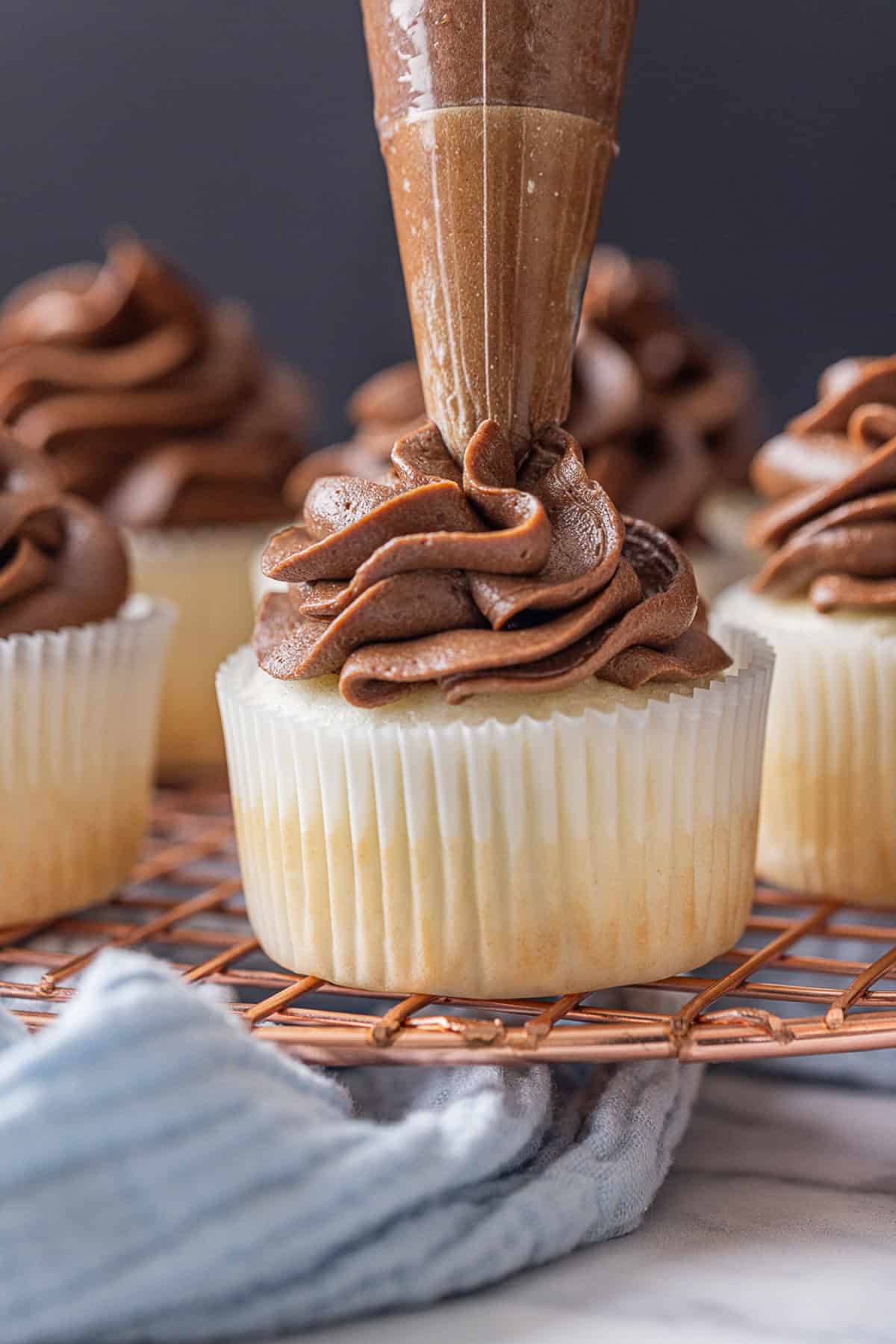 Piping chocolate cream cheese frosting on a cupcake