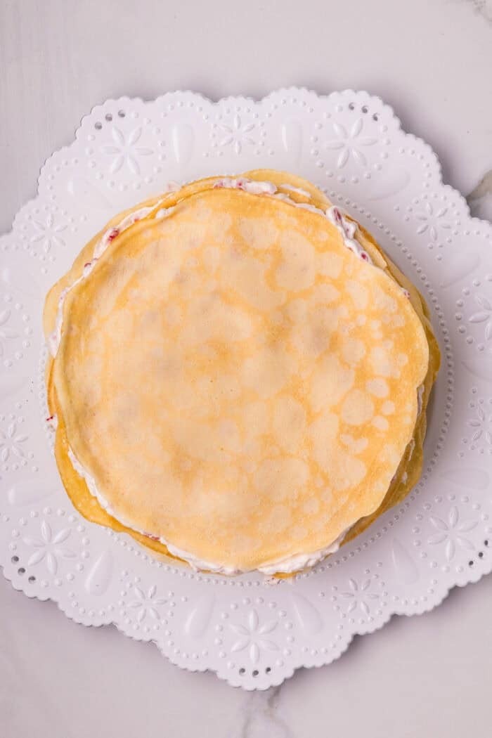 Crepes stacked on raspberry cream filling on a white plate