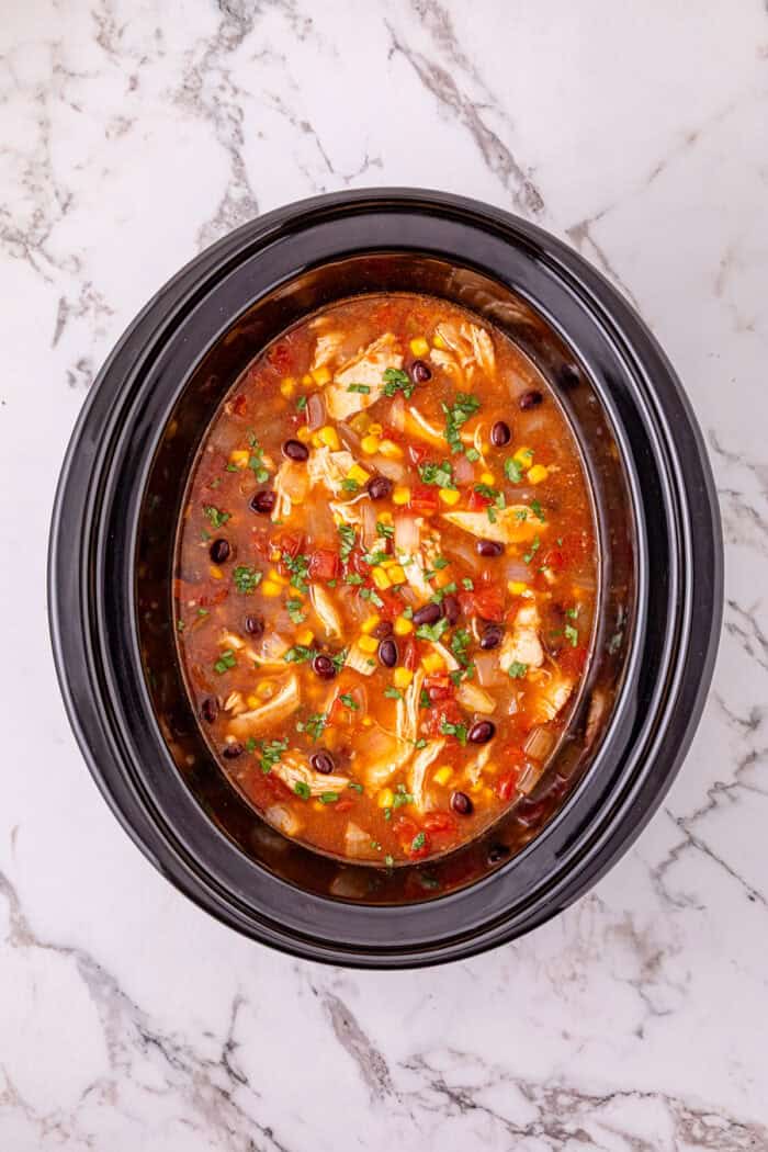 Chicken, beans, diced tomatoes and green chilies, and corn are slow-cooked in enchilada sauce broth to make Crockpot Chicken Enchilada Soup. Overhead view of chicken enchilada soup in the crockpot