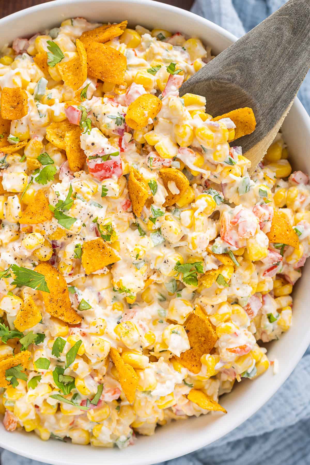 A wooden spoon in a bowl of Frito corn salad