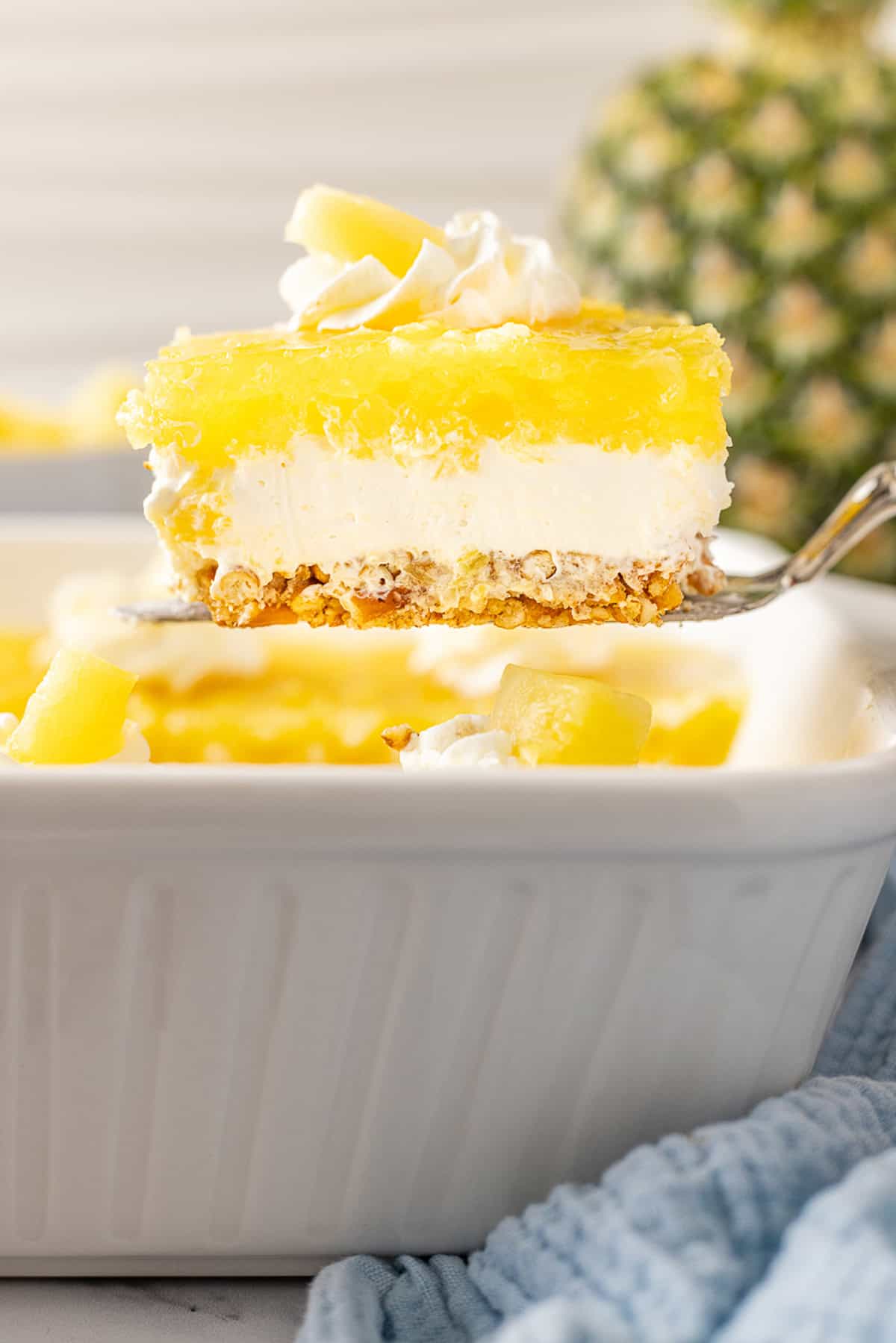 A salty pretzel crust, tangy cream cheese filling, and tart pineapple combine to make this Pineapple Pretzel Salad. Lifting a slice of pineapple pretzel salad from the baking dish