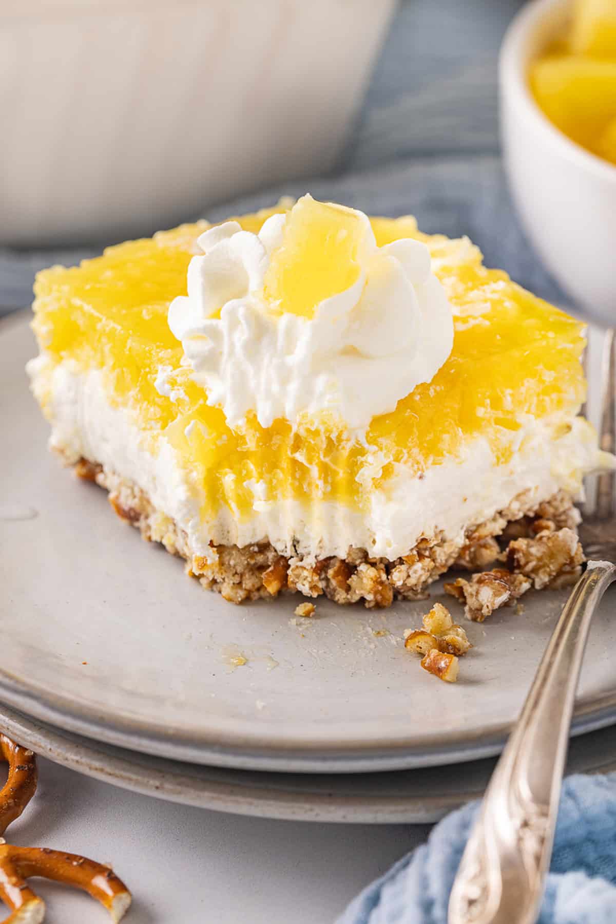 A salty pretzel crust, tangy cream cheese filling, and tart pineapple combine to make this Pineapple Pretzel Salad. A slice of pineapple pretzel salad on a plate with a bite missing