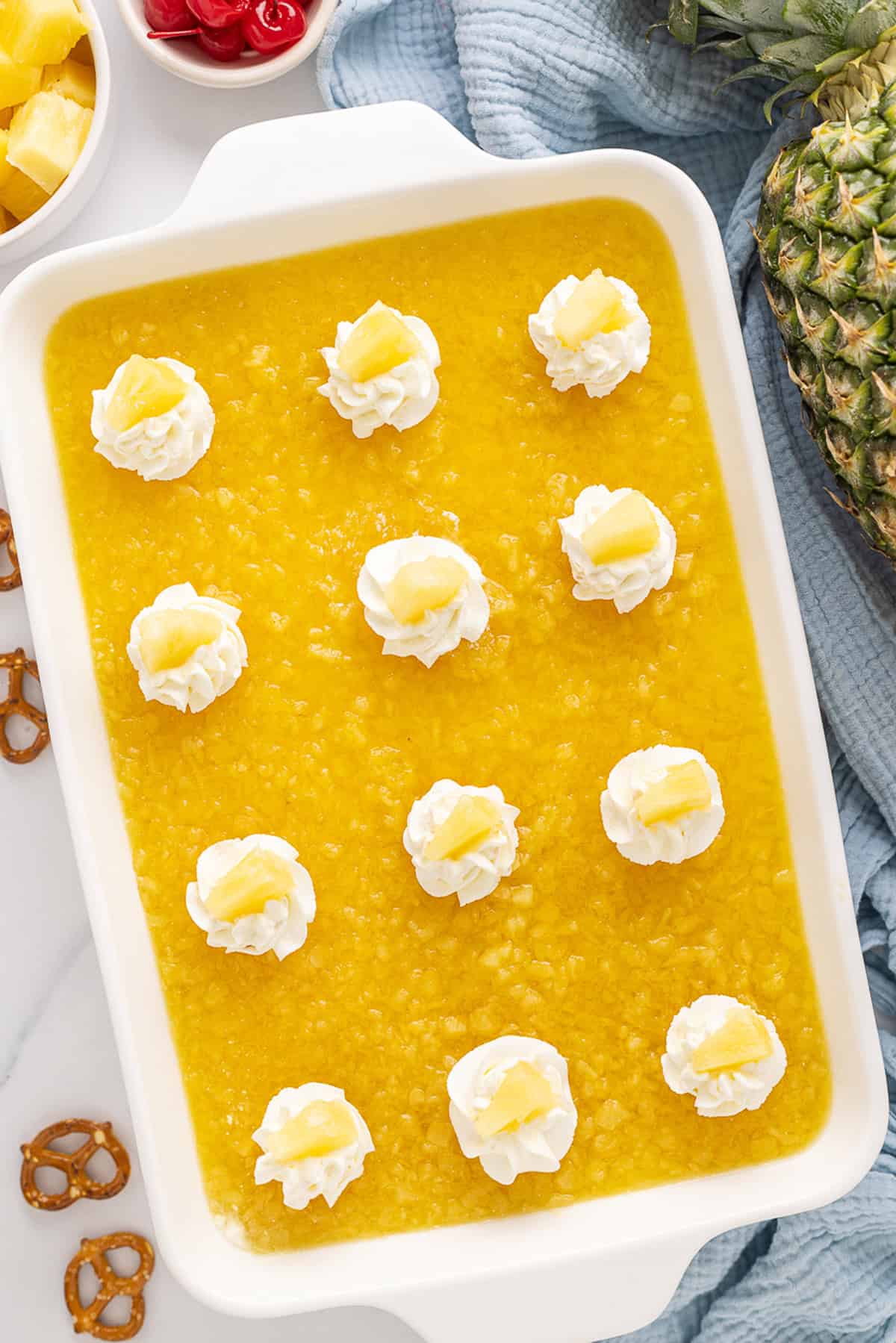 A salty pretzel crust, tangy cream cheese filling, and tart pineapple combine to make this Pineapple Pretzel Salad. Overhead view of a pineapple pretzel salad in a baking dish