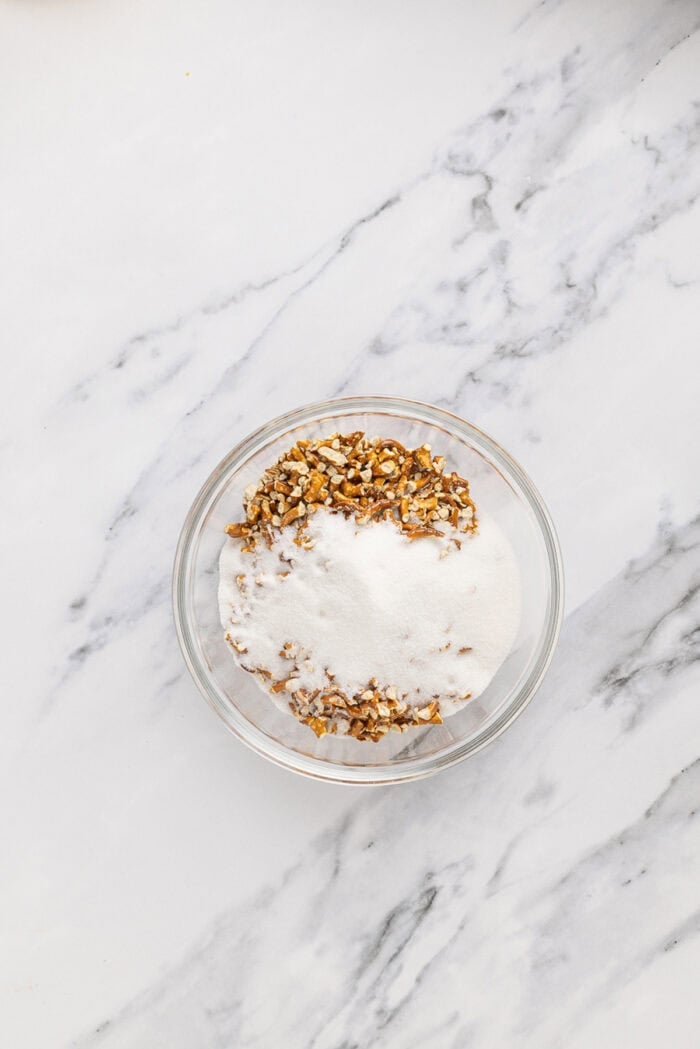 A salty pretzel crust, tangy cream cheese filling, and tart pineapple combine to make this Pineapple Pretzel Salad. Pretzel crumbs and sugar in a bowl