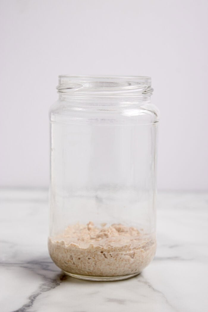 This easy sourdough starter recipe walks you through the process day-by-day with images. Great for beginners! Flour and white in a glass jar