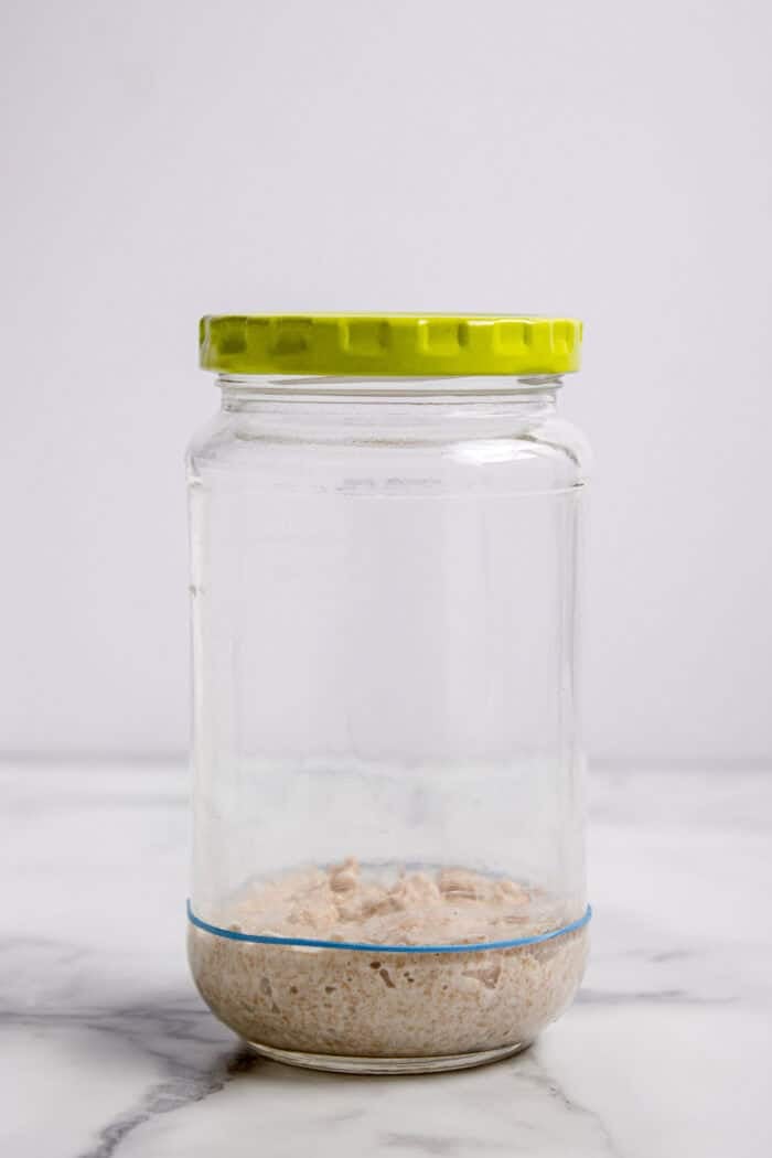 This easy sourdough starter recipe walks you through the process day-by-day with images. Great for beginners! Sourdough starter in a jar on day one