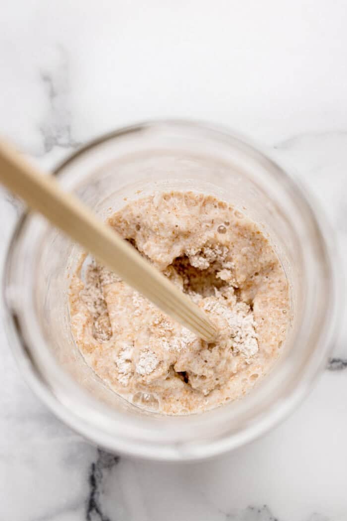 This easy sourdough starter recipe walks you through the process day-by-day with images. Great for beginners! Overhead view mixing flour and water in a glass jar