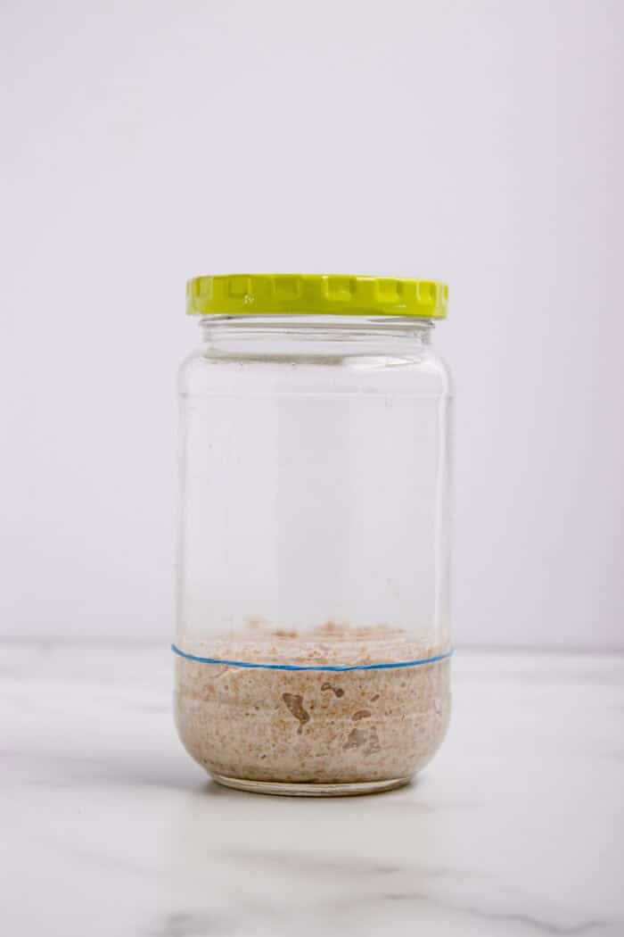 This easy sourdough starter recipe walks you through the process day-by-day with images. Great for beginners! Sourdough starter in a jar on the beginning of day 2 before it's risen