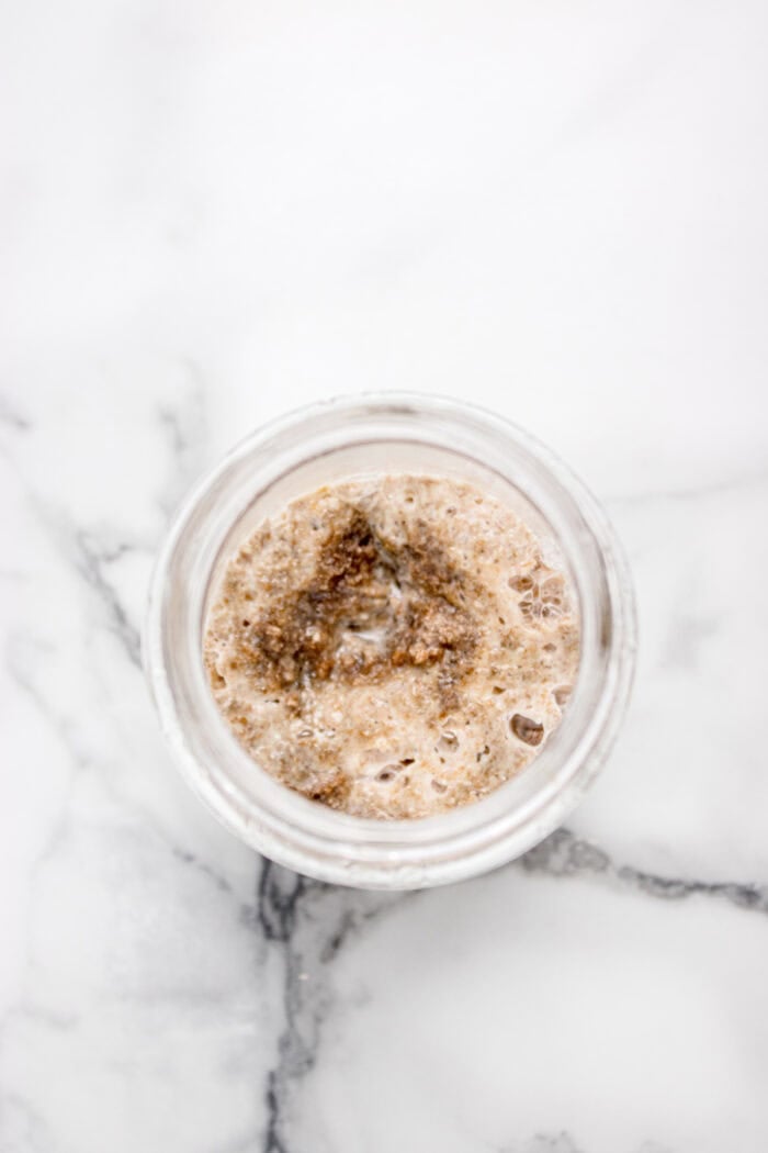 This easy sourdough starter recipe walks you through the process day-by-day with images. Great for beginners! Overhead view of a jar of sourdough starter on day 2