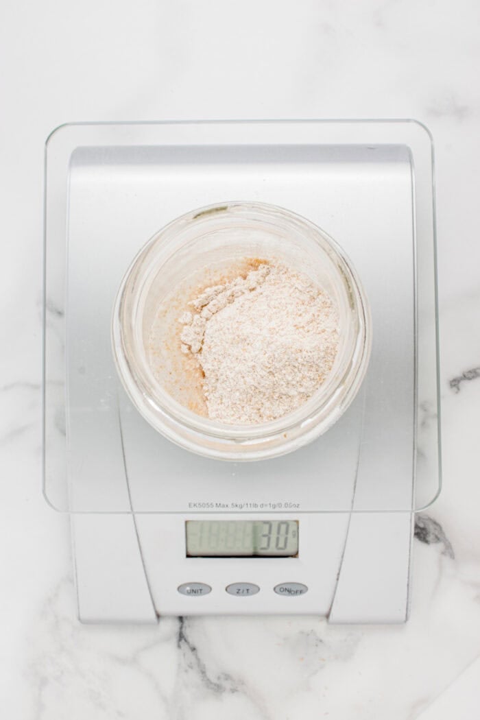 This easy sourdough starter recipe walks you through the process day-by-day with images. Great for beginners! Flour added to sourdough starter on a food scale