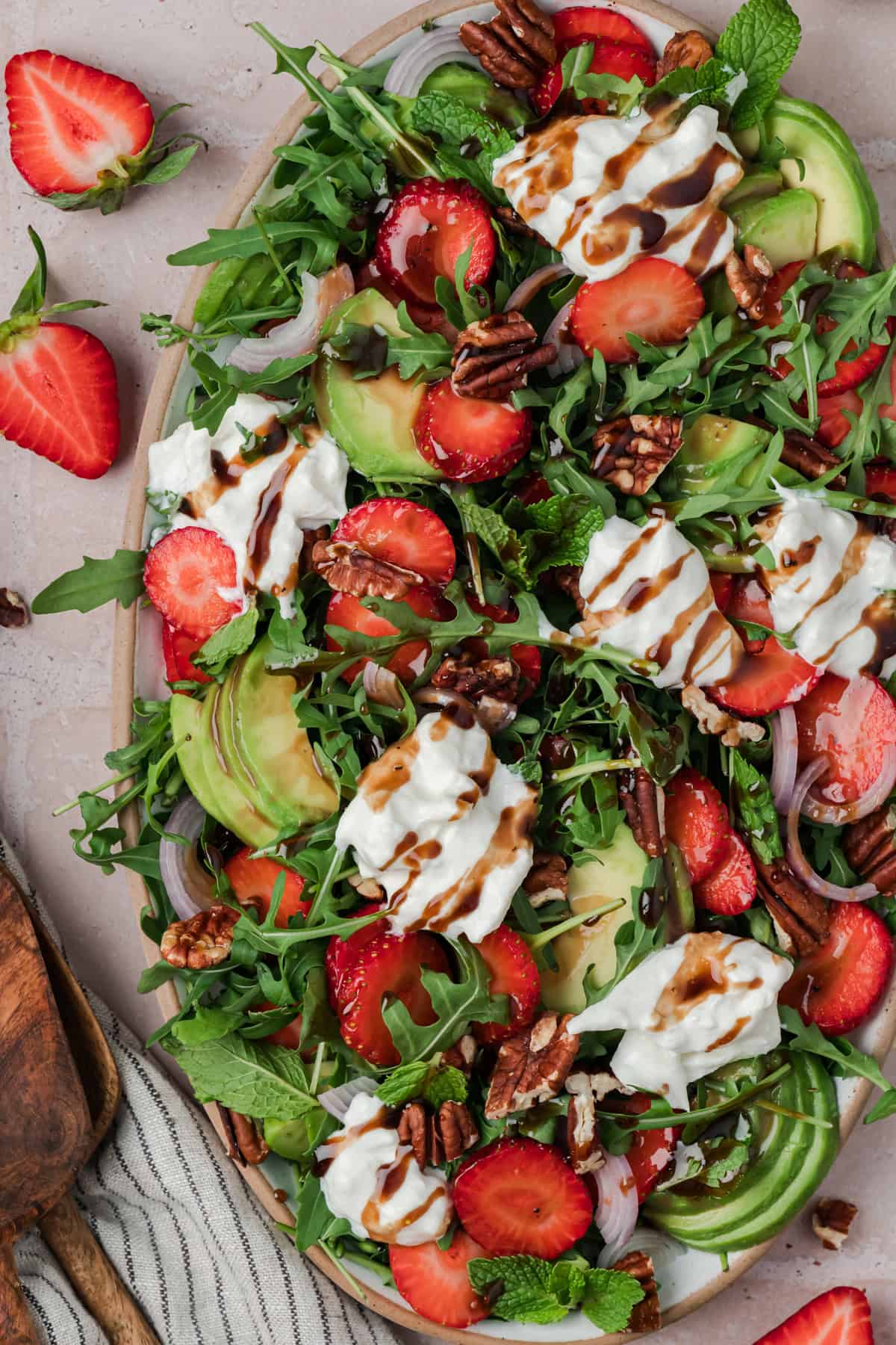 Strawberry Arugula Salad is perfect for summer, with peppery arugula, fresh strawberries, creamy burrata, crunchy pecans & avocado. Close up of strawberry arugula salad on a serving platter