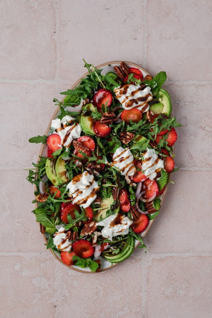Strawberry Arugula Salad is perfect for summer, with peppery arugula, fresh strawberries, creamy burrata, crunchy pecans & avocado. Burrata cheese and balsamic drizzle added to the salad