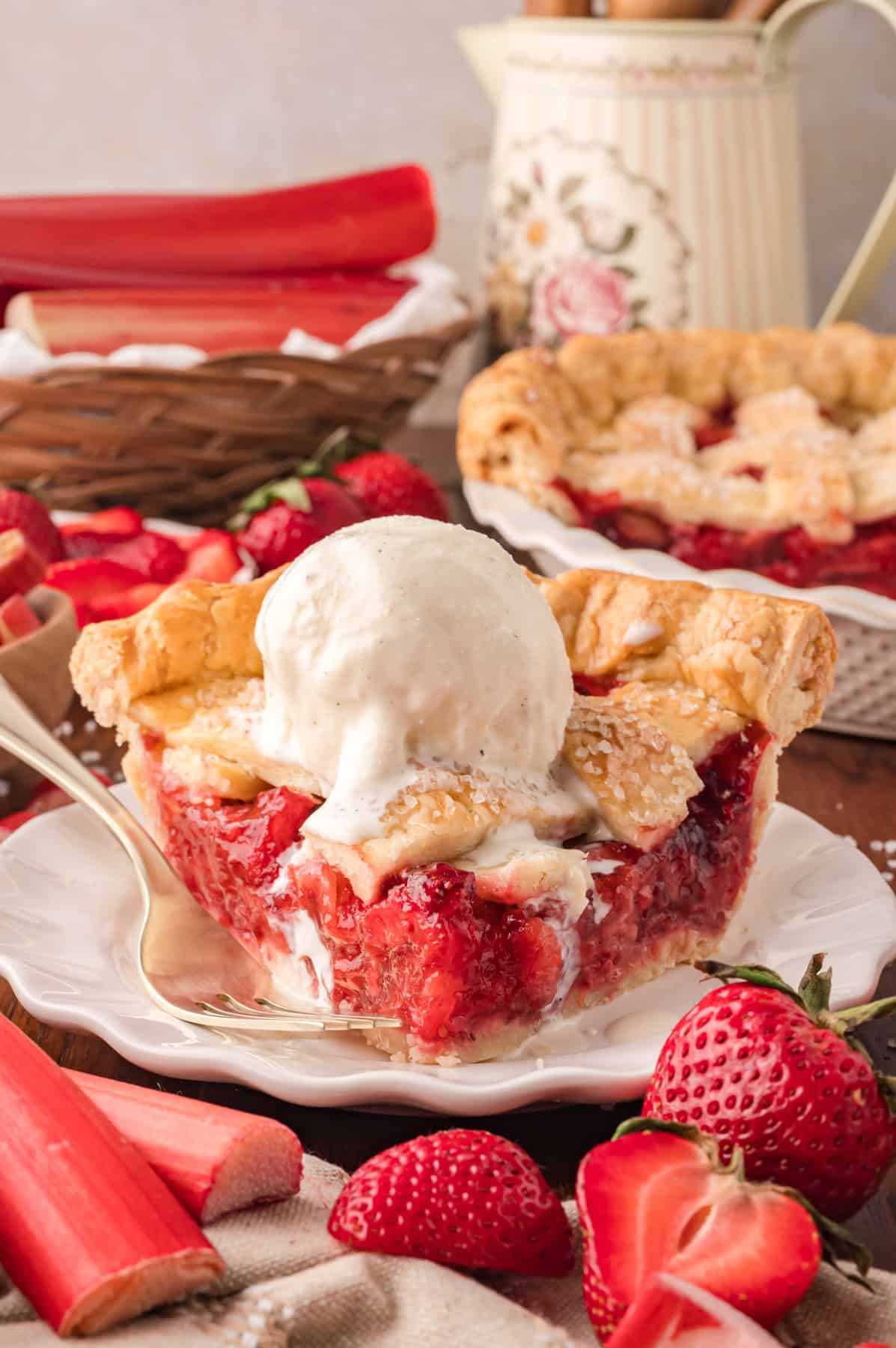 A slice of strawberry rhubarb pie on a white plate with a scoop of ice cream