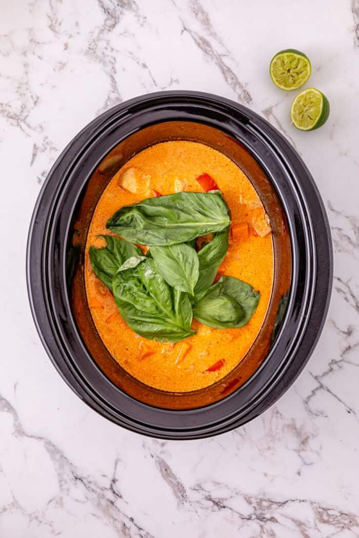 Chicken, sweet potatoes, coconut milk, curry paste, and peanut butter are slow-cooked to make this easy Thai Red Curry Chicken. Basil leaves on top of curry chicken in the crockpot