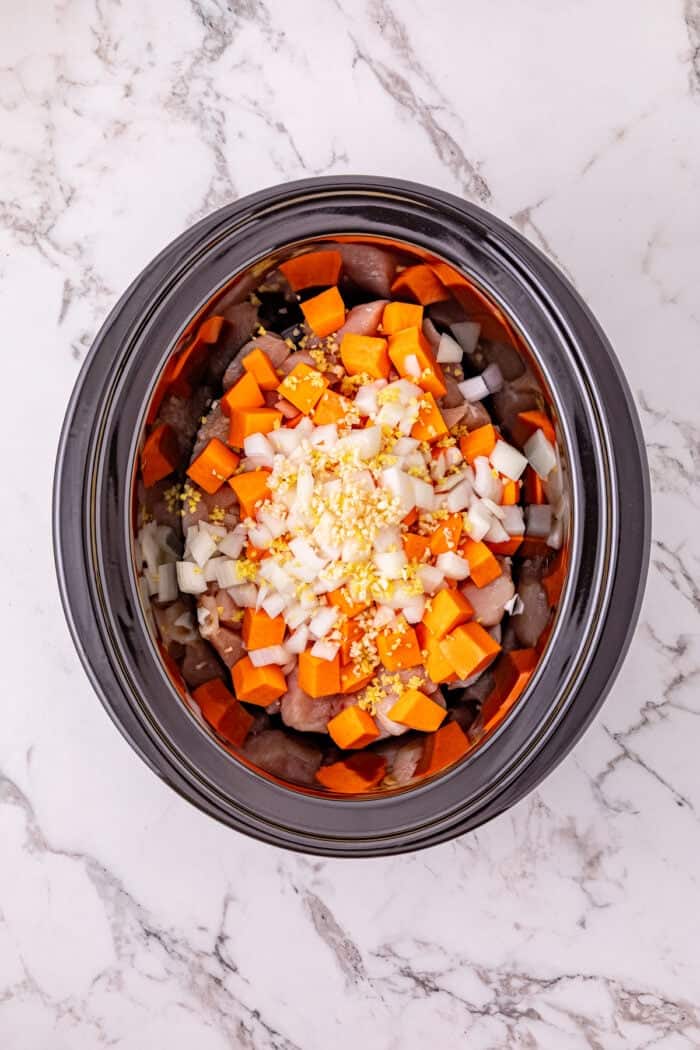 Chicken, sweet potatoes, coconut milk, curry paste, and peanut butter are slow-cooked to make this easy Thai Red Curry Chicken. Overhead view of chicken, sweet potatoes, and aromatics in the crockpot
