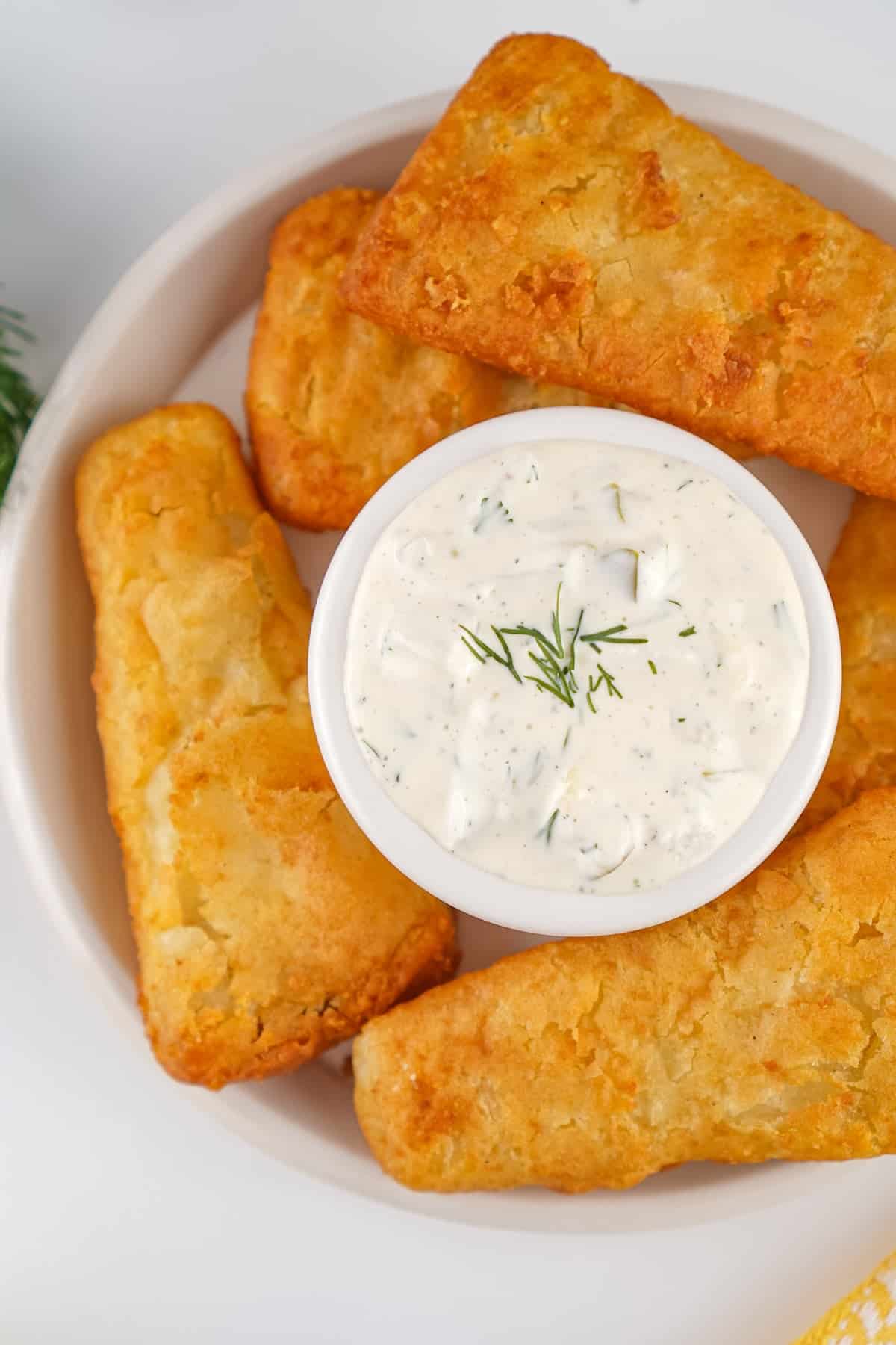 This easy Homemade Tartar Sauce recipe combines fresh dill, mayo, and pickles to create a creamy, tangy dip for seafood. Overhead view of a plate of fish sticks with a dish of tartar sauce in the center
