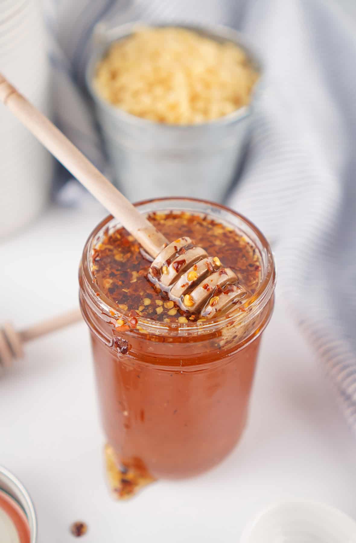 This Hot Honey recipe is made with just 3 ingredients in 7 minutes. It’s ridiculously easy and so much cheaper than buying it at the store. A honey stirrer in a jar of homemade hot honey