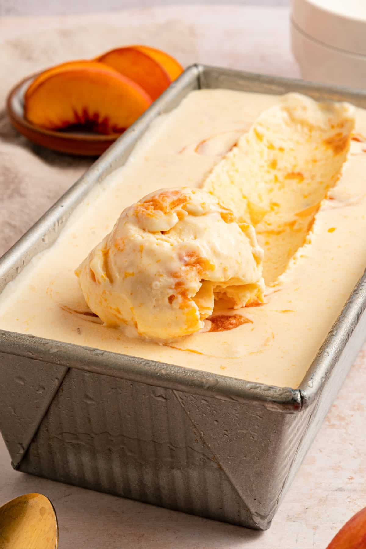 Fresh peaches are turned into a compote and swirled into a mixture of sweetened condensed milk & heavy cream in this No-Churn Peach Ice Cream. a scoop of peach ice cream in a pan