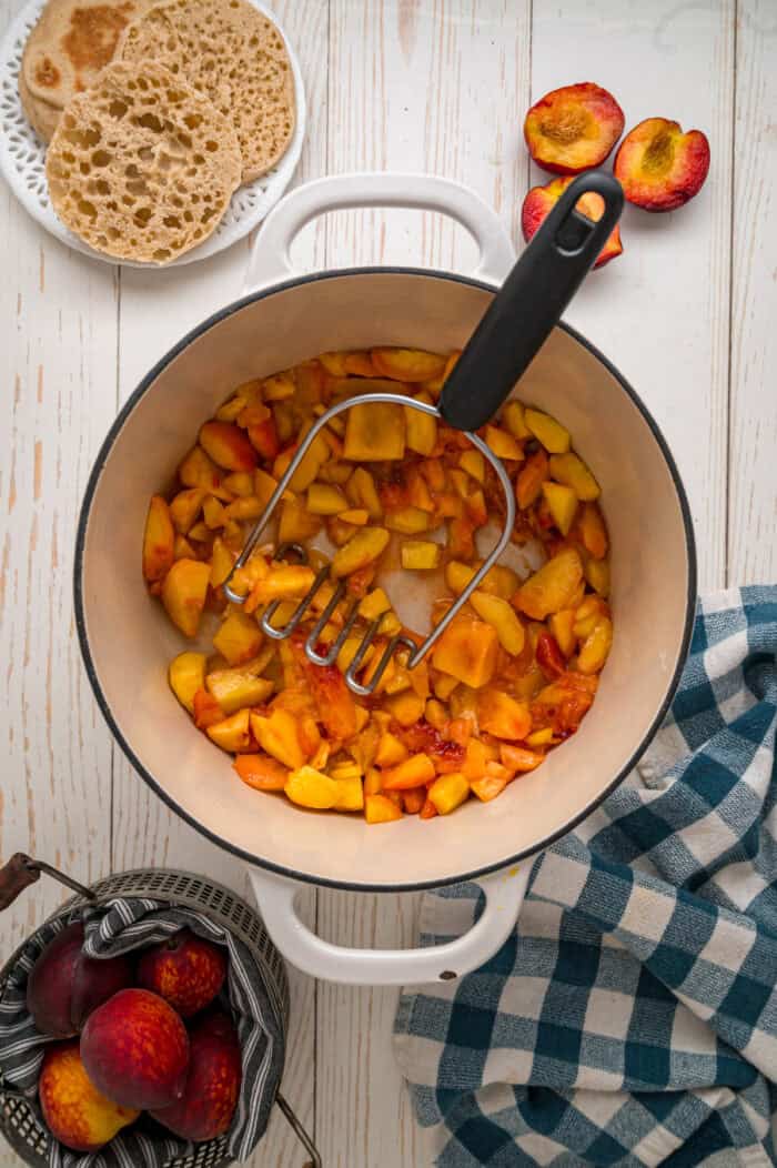 Mashing diced peaches in a pot