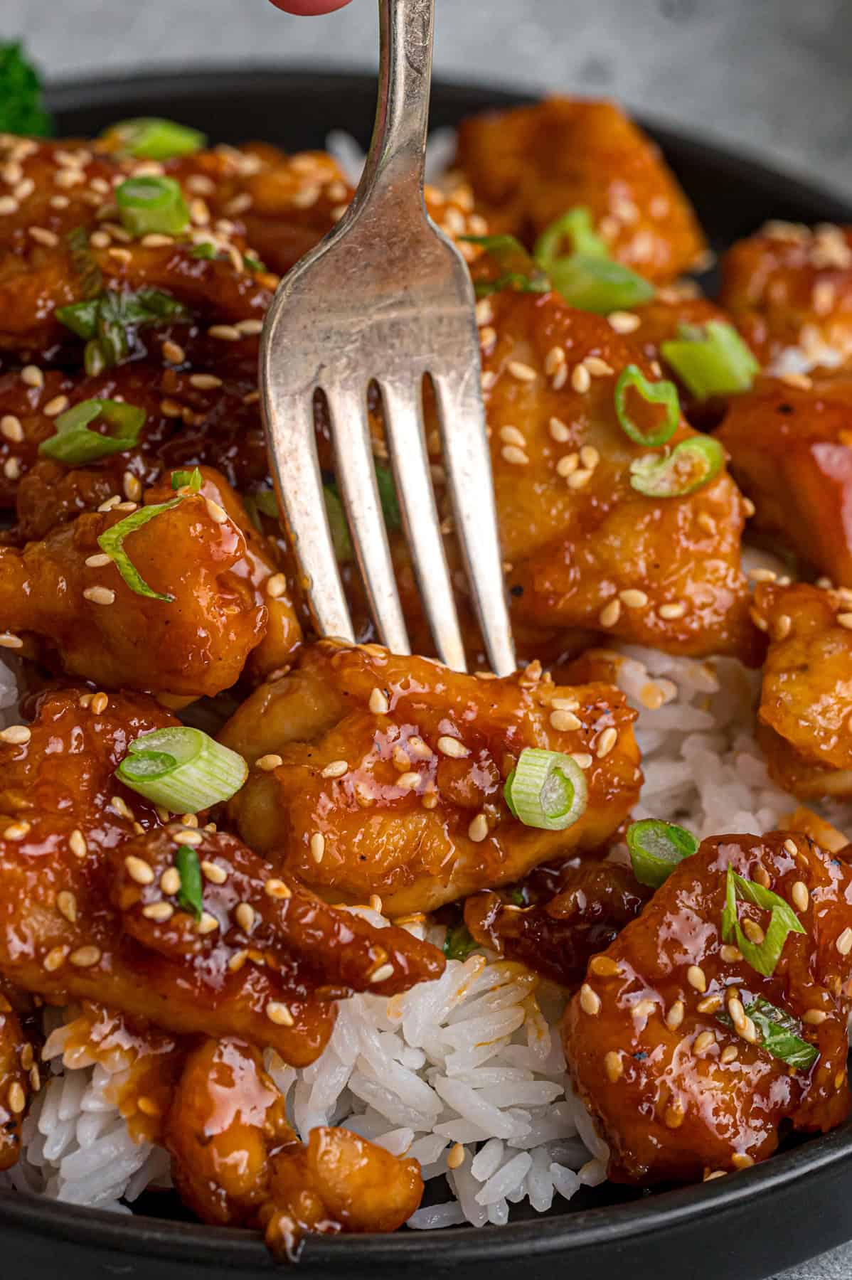 Ready in just 30 minutes, this Sesame Chicken recipe features tender, juicy pieces of chicken coated in a savory-sweet and nutty sauce. A fork in a piece of sesame chicken over rice