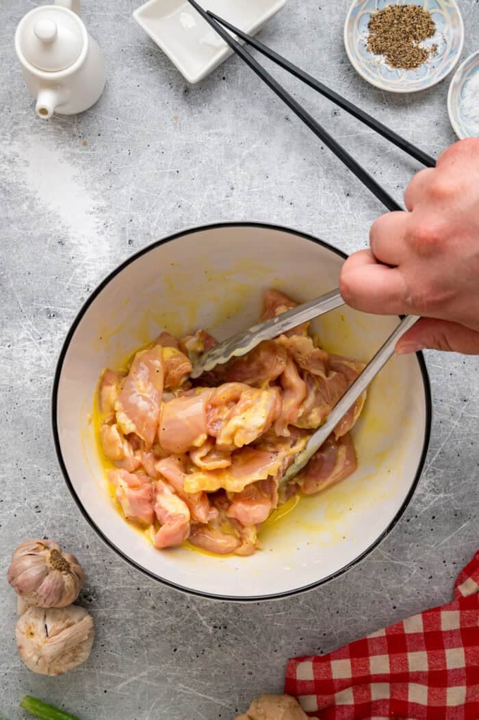 Ready in just 30 minutes, this Sesame Chicken recipe features tender, juicy pieces of chicken coated in a savory-sweet and nutty sauce. Tongs tossing pieces of chicken in an egg mixture