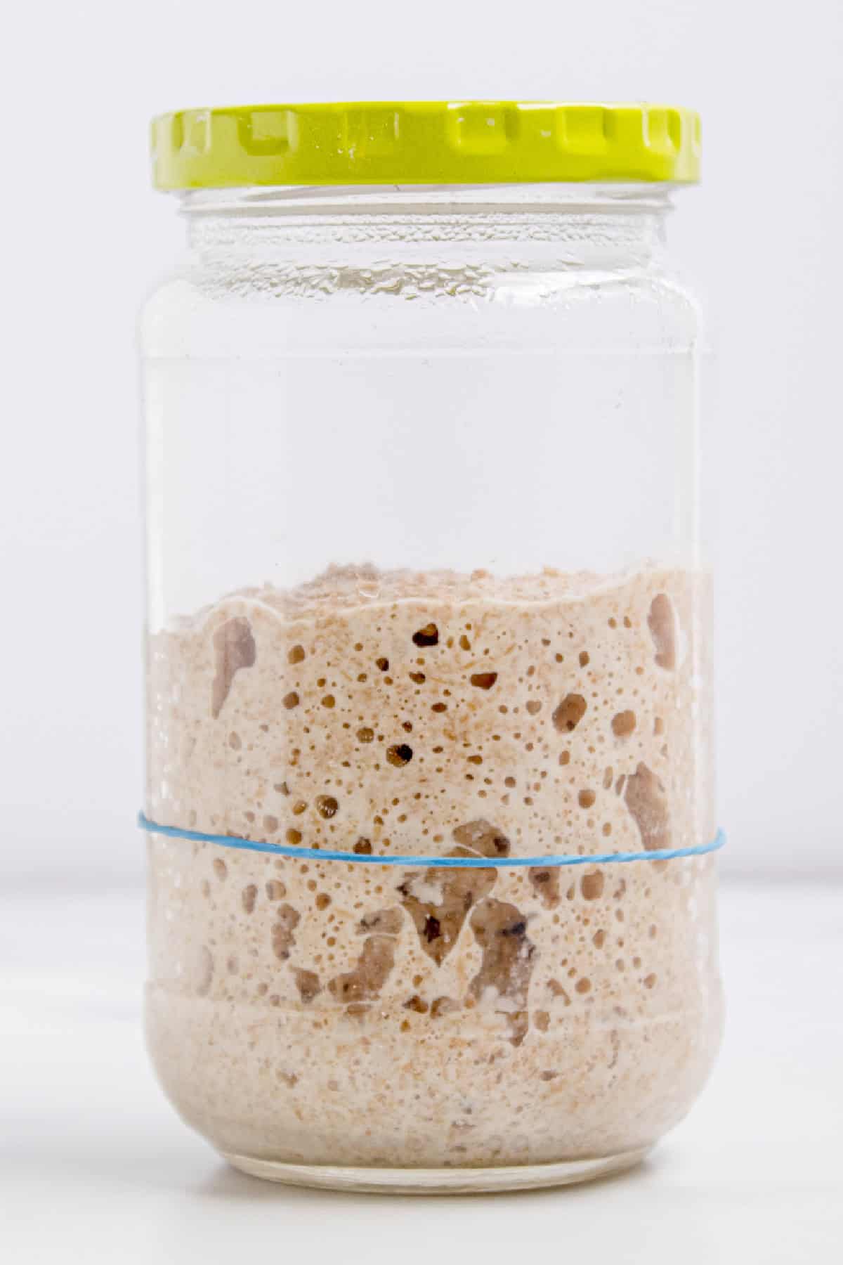 This easy sourdough starter recipe walks you through the process day-by-day with images. Great for beginners! Sourdough starter in a glass jar on day 8 that has doubled in size