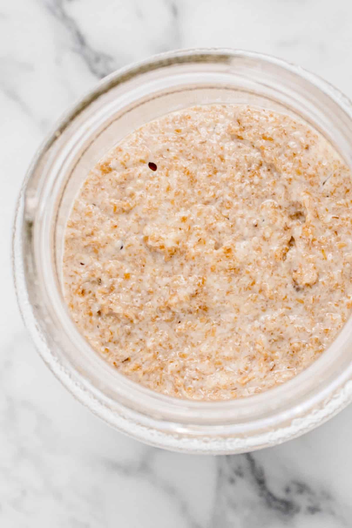 This easy sourdough starter recipe walks you through the process day-by-day with images. Great for beginners! Overhead view of sourdough starter in a glass jar on day 8